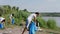 In a large green beach beside of the lake group of young guys and ladies volunteers cleaning the rubbish they picking up