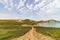 Large green field with a center road and bushes. Beautiful view of field with blue sky