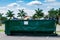 Large green metal dumpster filled with garbage in parking lot - Davie, Florida, USA