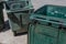 Large green trash cans, empty with lids open, curbside