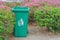 Large green wheelie bin at public park with bush.