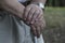 The large hands of an elderly man are folded on a cane with a watch on his right hand