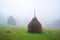 A large haystack stands on a green field among the dense gray fog