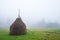 A large haystack stands on a green field among the dense gray fog