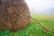 A large haystack stands on a green field among the dense gray fog