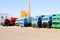 Large heavy cargo trucks with cabs and trailers stand in a row ready for delivery of cargo at the industrial refinery