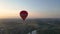 Large hot air balloon with basket flies over fields on a background of evening blue sky