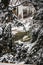 Large icicles hang off of a stony ridge over a small stream in the forest during the winter