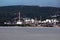 Large industrial complex filled with oil refinery tankers next to tall industrial chimney surrounded with dense forest and calm