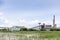 Large industrial factory building with conveyor and smokestack at water and green field on blue sky of bright day