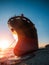 Large iron cargo ship run aground at sea bay at sunset. Industrial sea vessel shipwreck on coastline after storm accident