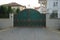 Large iron green gate with a brown forged pattern and a gray brick fence