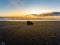 Large isolated black stone in the middle of the black sand beach of Reynisfjara illuminated by the last rays of sunset sun from