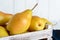 Large juicy yellow pears in a rustic wooden fruit box on a white table.