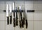 Large kitchen knives and honing steels hanging on a magnetic holder on the tiled wall, copy space