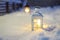 Large lantern with burning candle on street of small town during snowfall on Christmas eve. Stylish Xmas decorations among