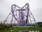 Large lilac amusement ride roller coaster on the plain fenced by a blue metal fence