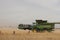 Large machinery harvesting a wheat crop on a farm in an agricultural, dry, windy and dusty farmland area near Melbourne,