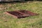 Large manhole cover made of strong rusted metal wire bars surrounded with uncut grass