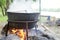 Large metal pot with a lid and handle on tripod used for cooking. Cooking in a bowler hat on the fire in nature