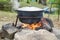 Large metal pot with a lid and handle on tripod used for cooking. Cooking in a bowler hat on the fire in nature