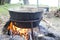 Large metal pot with a lid and handle on tripod used for cooking. Cooking in a bowler hat on the fire in nature