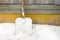 A large metal snow shovel stands against the wall