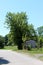 Large mighty tree rising high above small storage shed surrounded with rusted wire fence at abandoned industrial complex backyard