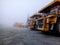 Large mining trucks are parked outside during fog.