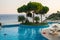 Large modern swimming pool with sun loungers and pine trees against the backdrop of the sea.