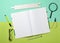 A large notebook for notes and drafting with stationery objects for a student on a green blue pastel background.