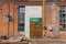 A large old dilapidated house of red and white bricks with large dilapidated windows and a multi-colored metal door. Old dirty