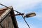 Large old dirty street lamp mounted on rusted metal pipe with new dark electrical wires on side of wooden barn roof