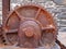 Large old rusty cogwheel on obsolete heavy machinery against a stone wall