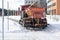 A large orange snowplow cleans snow from the pavement