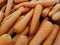 A large, orange stack of large fresh carrots, being sold in a store bin.