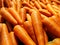 A large, orange stack of large fresh and healthy carrots, being sold in a large market.