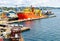 A large orange and yellow colored Offshore Construction Vessel OCV is in a dry dock of a shipyard and is being repaired