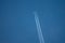 large passenger aircraft flies in the cloudless blue sky and produces a white glowing condensation trail
