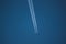 large passenger aircraft flies in the cloudless blue sky and produces a white glowing condensation trail