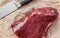 A large piece of raw beef meat next to a large kitchen knife on a background of food paper