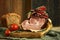 A large piece of succulent ham with two ripe tomatoes and basilico leaves arranged on a wooden plate. A piece of whole wheat bread