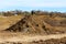 Large pile of dry soil mixed with rocks and construction material at local construction site in front of small hill