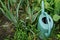 Large plastic watering can with water among green grass and vegetation