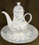 A large porcelain white teapot with blue flowers stands on a platter on the table against a black isolated background