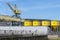 A large port crane on rails standing on the loading yard, visible yellow silos.