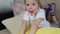 A large portrait of a little girl lying on a yellow pillow opens her mouth wide and shows her tongue.