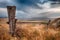 Large post at the end of a barbed wire fence in a high desert hilly setting