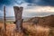 Large post at the end of a barbed wire fence in a high desert hilly setting