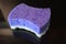 A large purple feminine washcloth for personal hygiene with a white massage surface is located on a black glossy surface.